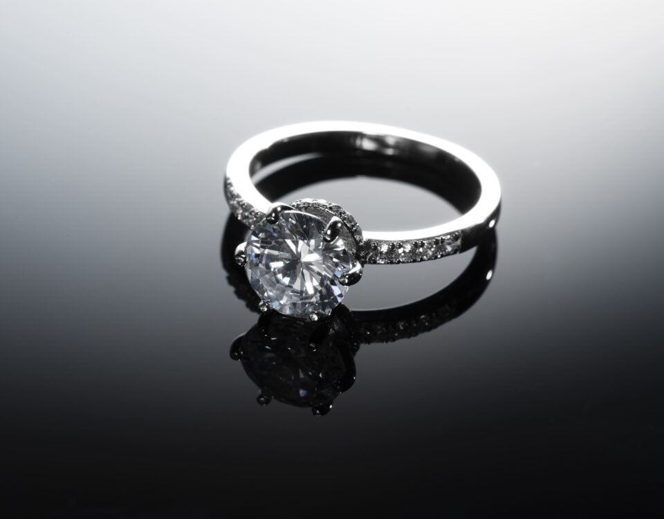 A stunning diamond engagement ring with a silver band placed on a reflective black surface, creating a luxurious and sophisticated look.