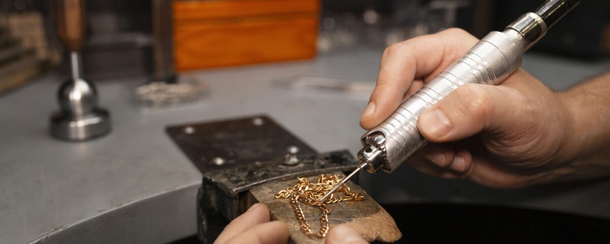 A skilled jeweler using a precision tool to solder a delicate gold chain, showcasing expert craftsmanship in handmade jewelry design.