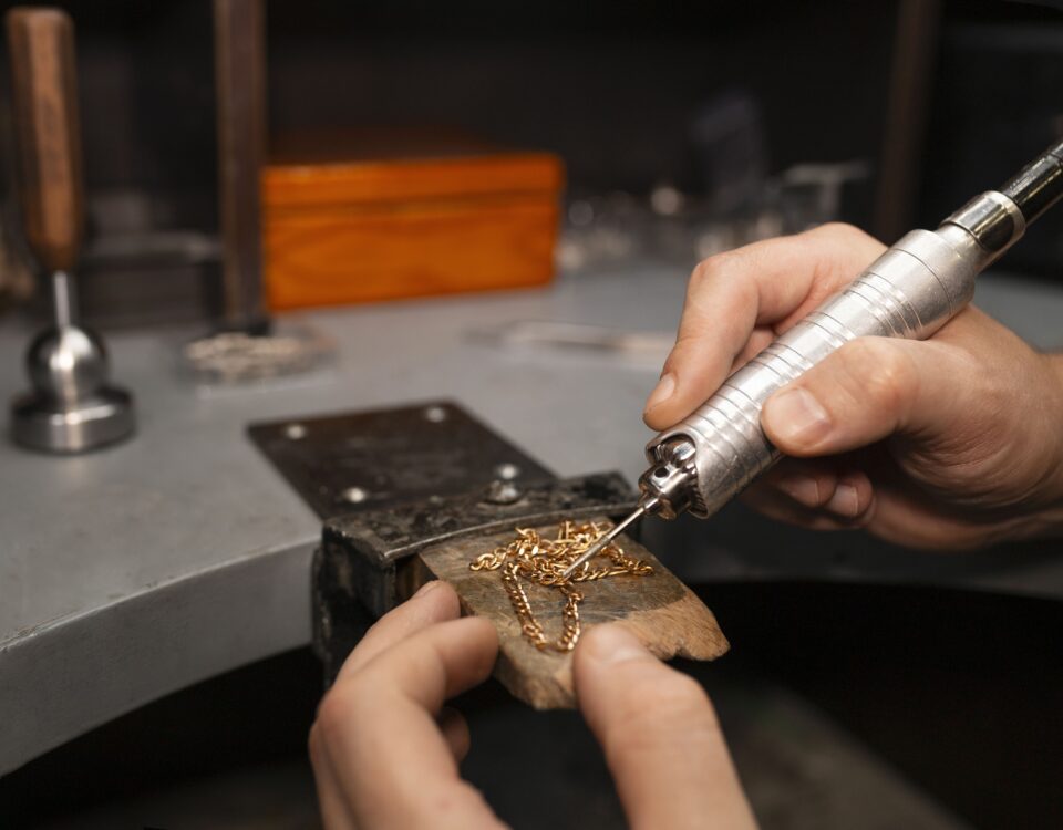 A skilled jeweler using a precision tool to solder a delicate gold chain, showcasing expert craftsmanship in handmade jewelry design.